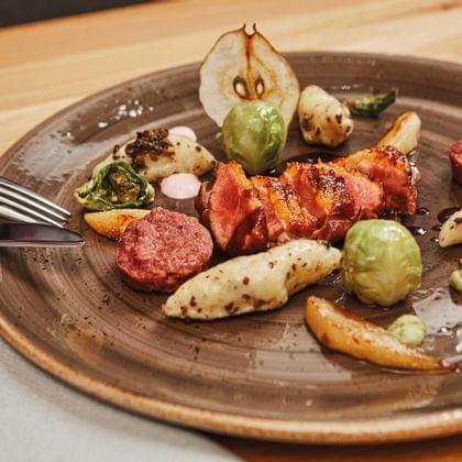 Gourmet-Fleischgericht mit Speck umwickeltem Schweinefleisch, Gnocchi, Rosenkohl und Birnenscheiben auf braunem Teller